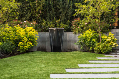 Diseño de jardín actual en patio trasero con adoquines de hormigón y fuente