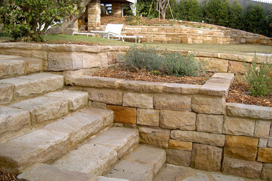 Imagen de jardín tradicional grande en patio trasero con exposición reducida al sol, adoquines de piedra natural y muro de contención