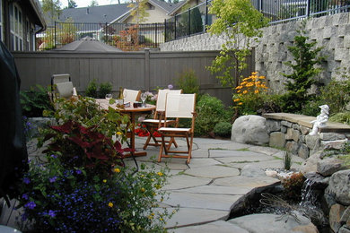 Foto de jardín clásico de tamaño medio en verano en patio trasero con jardín francés, muro de contención, adoquines de piedra natural y exposición total al sol