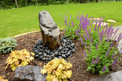 Ejemplo de jardín de tamaño medio en patio trasero con jardín francés, fuente y adoquines de piedra natural