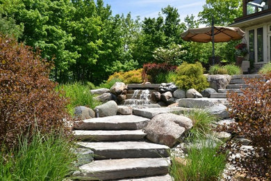 This is an example of a large rustic partial sun backyard stone water fountain landscape in Toronto.