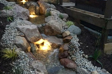This is an example of a large rustic partial sun backyard water fountain landscape in Grand Rapids.