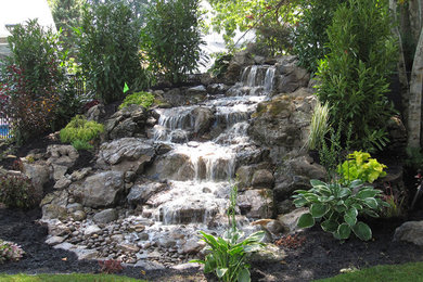 This is an example of a mid-sized tropical backyard stone water fountain landscape in New York.