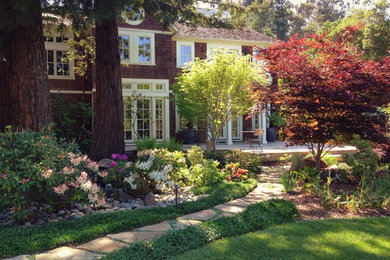 Exempel på en stor amerikansk trädgård i delvis sol, med en trädgårdsgång och naturstensplattor