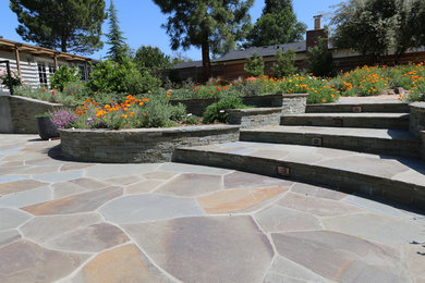 Réalisation d'un grand jardin arrière méditerranéen au printemps avec des pavés en pierre naturelle, un mur de soutènement et une exposition ensoleillée.