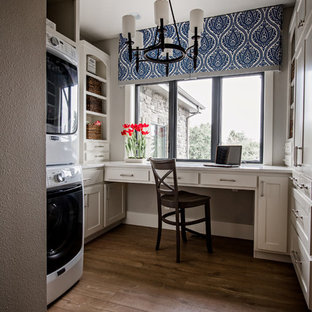 Ejemplo de lavadero multiusos y en U, de estilo de casa de campo, con armarios estilo shaker, puertas de armario beige, suelo de madera oscura, lavadora y secadora apiladas, suelo marrón y paredes grises