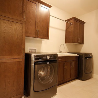 Esempio di una grande sala lavanderia classica con lavatoio, ante in stile shaker, ante in legno bruno, top in laminato, pareti beige, pavimento con piastrelle in ceramica, lavatrice e asciugatrice affiancate e pavimento beige