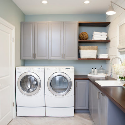 Example of a large classic l-shaped porcelain tile dedicated laundry room design in New York with raised-panel cabinets, gray cabinets, wood countertops, blue walls, a side-by-side washer/dryer, a drop-in sink and brown countertops
