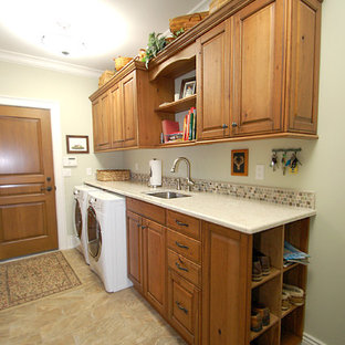 Réalisation d'une buanderie linéaire tradition dédiée et de taille moyenne avec un évier encastré, un placard avec porte à panneau surélevé, des portes de placard en bois brun, un plan de travail en granite, une crédence beige, une crédence en mosaïque, un sol en carrelage de porcelaine, un mur vert et des machines côte à côte.