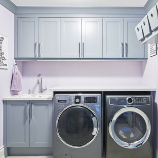 Cette photo montre une buanderie linéaire tendance multi-usage et de taille moyenne avec un évier encastré, un placard à porte shaker, des portes de placard grises, un plan de travail en quartz modifié, un mur violet, un sol en carrelage de porcelaine, des machines côte à côte, un sol blanc et un plan de travail blanc.