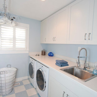 Réalisation d'une grand buanderie linéaire tradition dédiée avec un plan de travail en stratifié, un évier posé, des portes de placard blanches, un placard à porte shaker, un mur bleu, un sol en linoléum, des machines côte à côte, un sol multicolore et un plan de travail blanc.
