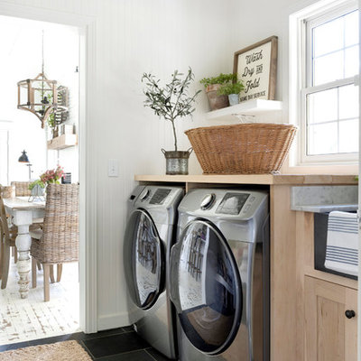 Inspiration for a farmhouse black floor laundry room remodel in Minneapolis with shaker cabinets, light wood cabinets, wood countertops, white walls, a side-by-side washer/dryer and beige countertops