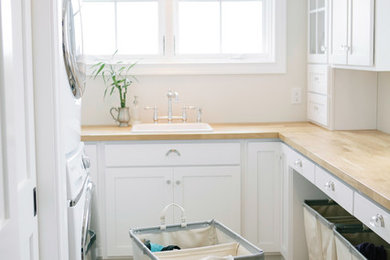 Inspiration for a timeless u-shaped dedicated laundry room remodel in Boston with a drop-in sink, shaker cabinets, white cabinets, white walls, a stacked washer/dryer and beige countertops