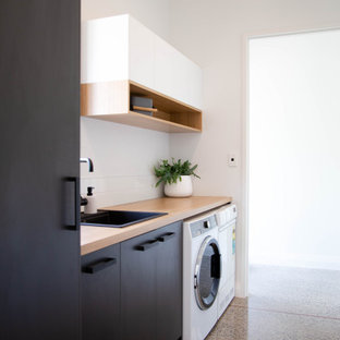 Idéer för att renovera ett mellanstort funkis linjärt grovkök, med en nedsänkt diskho, släta luckor, svarta skåp, laminatbänkskiva, vita väggar, betonggolv och en tvättmaskin och torktumlare bredvid varandra