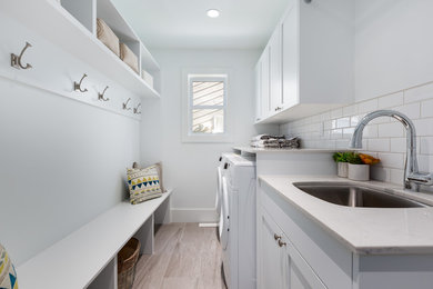 Beach style galley porcelain tile and gray floor utility room photo in Vancouver with an undermount sink, shaker cabinets, white cabinets, quartz countertops, white walls and a side-by-side washer/dryer