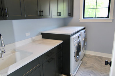Example of a mid-sized farmhouse galley porcelain tile dedicated laundry room design in Chicago with an undermount sink, raised-panel cabinets, gray cabinets, quartz countertops, a concealed washer/dryer and white countertops