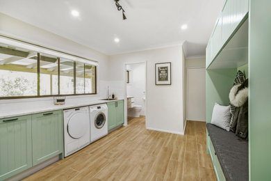 シドニーにあるトラディショナルスタイルのおしゃれな家事室 (アンダーカウンターシンク、シェーカースタイル扉のキャビネット、緑のキャビネット、ラミネートカウンター、グレーの壁、磁器タイルの床、左右配置の洗濯機・乾燥機、茶色い床) の写真