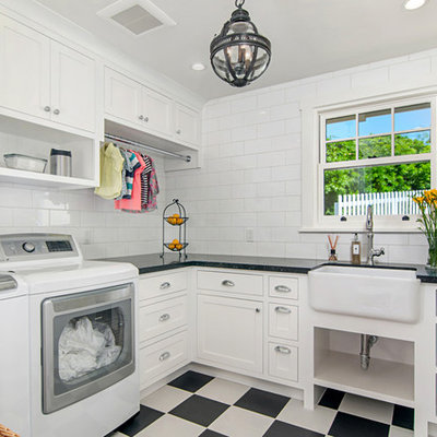 Inspiration for a small timeless l-shaped linoleum floor and multicolored floor dedicated laundry room remodel in San Diego with a farmhouse sink, white cabinets, white walls, a side-by-side washer/dryer, black countertops and shaker cabinets