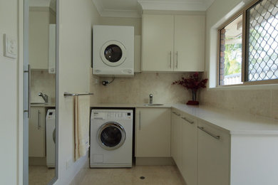 Moderne Waschküche in L-Form mit Unterbauwaschbecken, Quarzwerkstein-Arbeitsplatte, Marmorboden, Waschmaschine und Trockner gestapelt und grauen Schränken in Brisbane