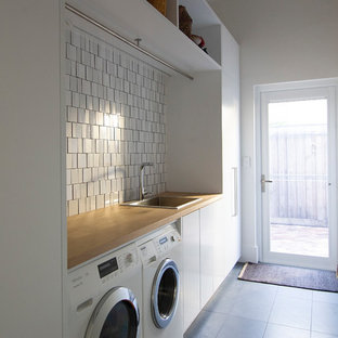 Ispirazione per una sala lavanderia minimal con lavello da incasso, ante lisce, ante bianche, top in legno, pareti bianche, pavimento in ardesia, lavatrice e asciugatrice affiancate, pavimento grigio e top marrone