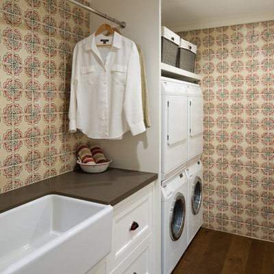 Example of a country galley dark wood floor dedicated laundry room design in San Diego with a farmhouse sink, multicolored walls, a stacked washer/dryer, white cabinets and recessed-panel cabinets