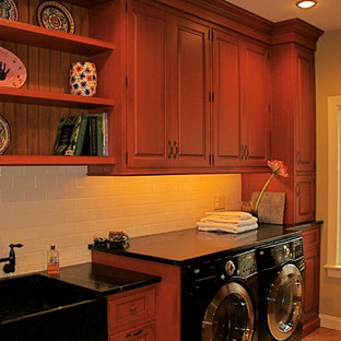 Immagine di una grande sala lavanderia chic con lavello stile country, ante con bugna sagomata, ante in legno scuro, pareti marroni, lavatrice e asciugatrice affiancate e pavimento beige