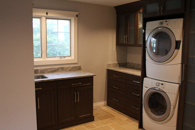 Klassisk inredning av en liten bruna l-formad brunt tvättstuga enbart för tvätt, med en undermonterad diskho, skåp i mörkt trä, granitbänkskiva, grå väggar, en tvättpelare, beiget golv, skåp i shakerstil och betonggolv