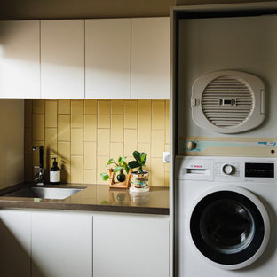 Idee per una sala lavanderia design di medie dimensioni con ante lisce, paraspruzzi con piastrelle in ceramica, top in quarzo composito, lavello sottopiano, ante bianche, paraspruzzi giallo, pavimento in ardesia, lavatrice e asciugatrice a colonna, pavimento multicolore e top marrone