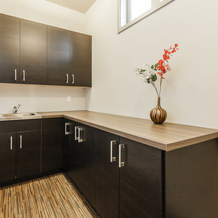 Inredning av ett modernt beige l-format beige grovkök, med en allbänk, släta luckor, laminatbänkskiva, beige väggar, bambugolv, tvättmaskin och torktumlare byggt in i ett skåp och skåp i mörkt trä