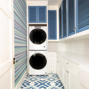 Idee per una lavanderia classica con lavello stile country, ante a persiana, ante blu, pareti multicolore, lavatrice e asciugatrice a colonna, pavimento multicolore, top bianco e carta da parati