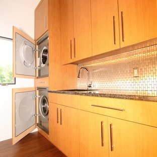 Immagine di una lavanderia minimalista con lavello sottopiano, ante lisce, top in granito, pareti bianche, pavimento in bambù e lavatrice e asciugatrice a colonna