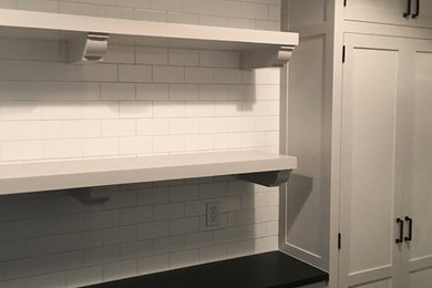 ニューヨークにある高級な中くらいなトランジショナルスタイルのおしゃれな洗濯室 (I型、落し込みパネル扉のキャビネット、白いキャビネット、人工大理石カウンター、白い壁、上下配置の洗濯機・乾燥機、スレートの床) の写真