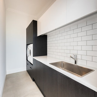 Idées déco pour une grand buanderie parallèle contemporaine avec un évier encastré, un placard à porte plane, des portes de placard noires, un plan de travail en marbre, une crédence blanche, une crédence en marbre, béton au sol et un sol marron.