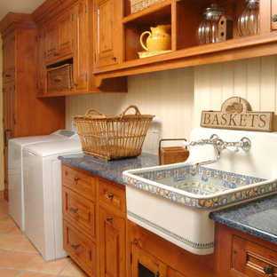 Immagine di una sala lavanderia country con lavello stile country, ante con bugna sagomata, ante in legno scuro, pareti beige, pavimento in terracotta, lavatrice e asciugatrice affiancate, pavimento arancione e top blu