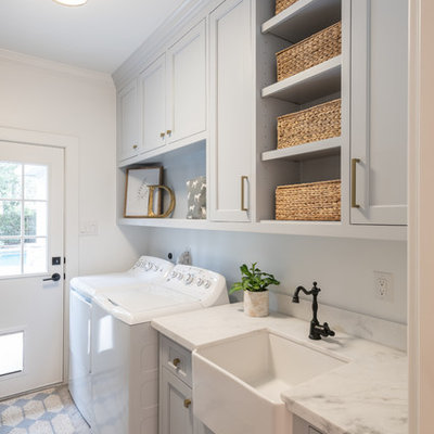 Dedicated laundry room - country single-wall gray floor dedicated laundry room idea in Houston with a farmhouse sink, recessed-panel cabinets, gray cabinets, white walls, a side-by-side washer/dryer and white countertops