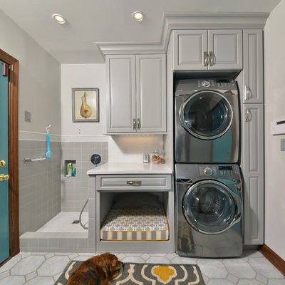 Mid-sized elegant single-wall porcelain tile and gray floor utility room photo in Cleveland with an utility sink, raised-panel cabinets, gray cabinets, quartz countertops, gray walls and a stacked washer/dryer