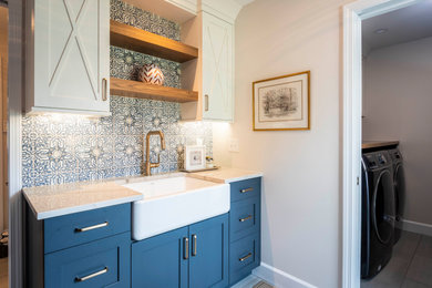 Example of a large transitional porcelain tile and gray floor utility room design in Indianapolis with a farmhouse sink, shaker cabinets, blue cabinets, quartz countertops, white walls, a side-by-side washer/dryer and white countertops