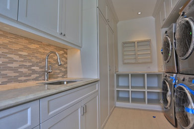 Huge minimalist dedicated laundry room photo in New York with an undermount sink, shaker cabinets, granite countertops, white walls and a side-by-side washer/dryer