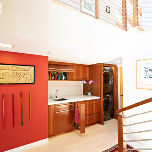 Ispirazione per una piccola lavanderia multiuso moderna con lavello sottopiano, ante lisce, ante in legno scuro, top in quarzo composito, pareti rosse, parquet chiaro, lavatrice e asciugatrice nascoste, pavimento marrone e top bianco