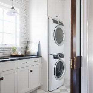 Réalisation d'une petit buanderie linéaire tradition multi-usage avec un évier encastré, un placard à porte shaker, des portes de placard grises, un plan de travail en granite, un mur blanc, des machines superposées, un sol multicolore, un plan de travail noir et béton au sol.