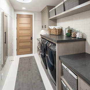 Bild på en stor lantlig grå parallell grått tvättstuga enbart för tvätt, med granitbänkskiva, skiffergolv, en tvättmaskin och torktumlare bredvid varandra, grått golv, luckor med infälld panel, grå skåp och grå väggar