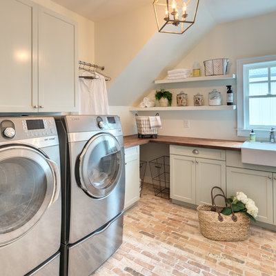 Inspiration for a country l-shaped brick floor and brown floor dedicated laundry room remodel in Atlanta with a farmhouse sink, shaker cabinets, green cabinets, wood countertops, white walls, a side-by-side washer/dryer and brown countertops