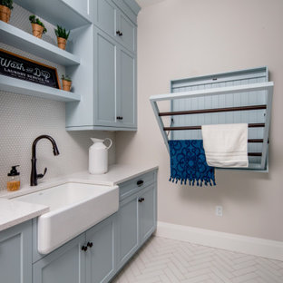 Esempio di una sala lavanderia country di medie dimensioni con lavello stile country, ante in stile shaker, ante blu, top in quarzo composito, paraspruzzi grigio, paraspruzzi con piastrelle in ceramica, pareti beige, lavatrice e asciugatrice a colonna, pavimento bianco e top bianco
