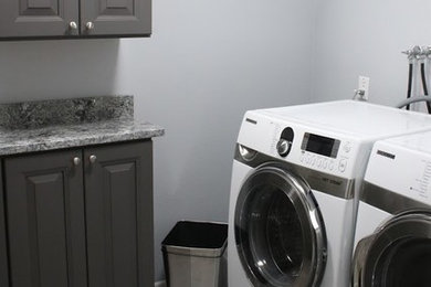 シアトルにある中くらいなトランジショナルスタイルのおしゃれな洗濯室 (コの字型、アンダーカウンターシンク、レイズドパネル扉のキャビネット、グレーのキャビネット、御影石カウンター、白い壁、左右配置の洗濯機・乾燥機、グレーのキッチンカウンター) の写真