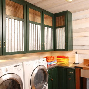 Foto de cuarto de lavado en L, rústico, grande, con puertas de armario verdes, paredes blancas, lavadora y secadora juntas, encimera de acero inoxidable y suelo de madera en tonos medios