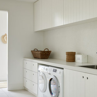Inspiration för en nordisk grå grått tvättstuga enbart för tvätt, med en enkel diskho, vita skåp, vita väggar, en tvättmaskin och torktumlare bredvid varandra och grått golv