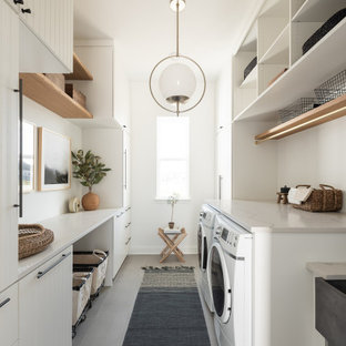 Bild på en stor vintage beige parallell beige tvättstuga enbart för tvätt, med en rustik diskho, vita skåp, vita väggar, släta luckor, en tvättmaskin och torktumlare bredvid varandra och grått golv