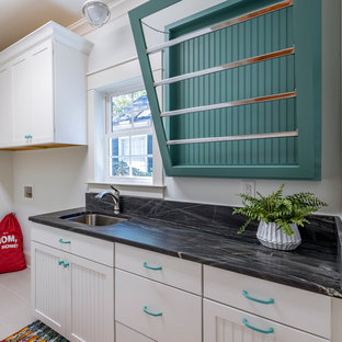 Inspiration för mellanstora klassiska linjära svart grovkök, med en undermonterad diskho, luckor med infälld panel, vita skåp, granitbänkskiva, vita väggar, klinkergolv i keramik och en tvättmaskin och torktumlare bredvid varandra