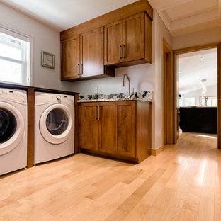 Esempio di una sala lavanderia chic di medie dimensioni con ante in stile shaker, ante in legno scuro, top in granito, pareti bianche, parquet chiaro e lavatrice e asciugatrice affiancate