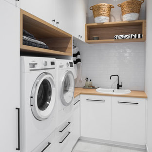 Inspiration för en liten maritim bruna l-formad brunt tvättstuga enbart för tvätt, med en nedsänkt diskho, vita skåp, träbänkskiva, vita väggar, klinkergolv i keramik, en tvättmaskin och torktumlare bredvid varandra, släta luckor och grått golv